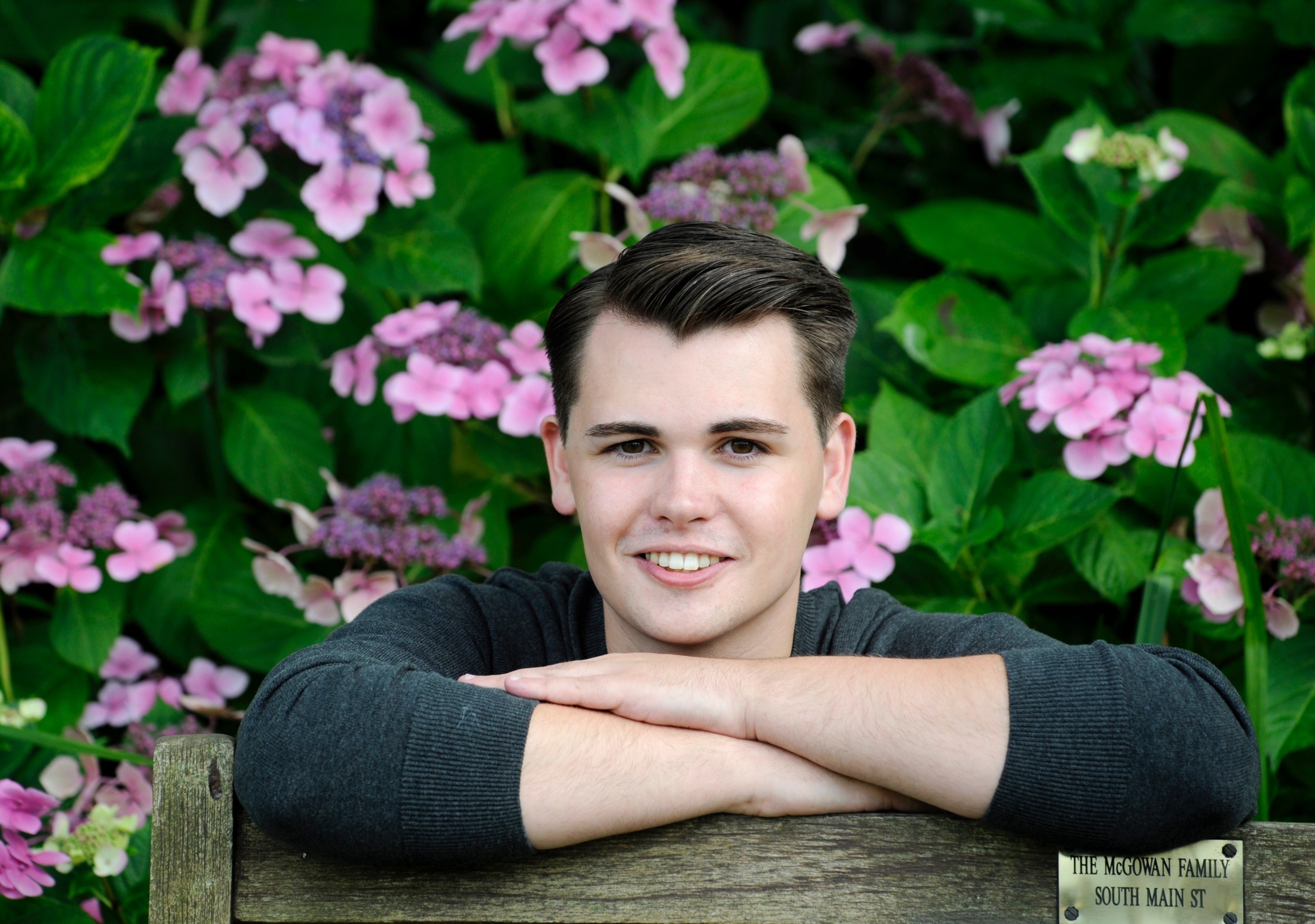 Andy Stewart, Children and Young People's Producer, in front of a pink hydrangea bush in Wigtown gardens with his arms folded in front of him.