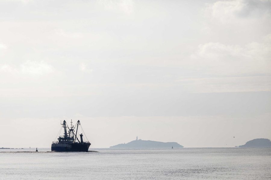 A fishing trawler out at sea. A lighthouse on a small island in the distance.