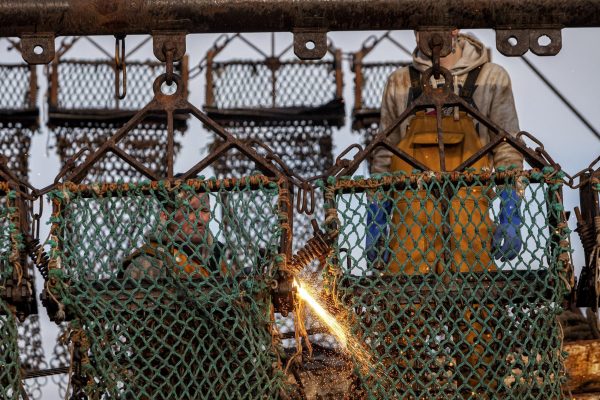 A person is welding a scallop dredger for a fishing trawler. Another person is looking on.