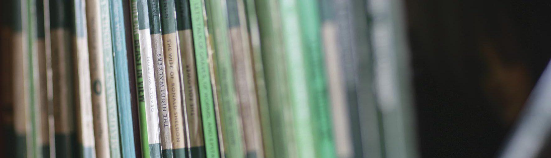 A row of vintage books on a bookshelf in one of Wigtown's second hand bookshops. Most are green and white, a range of penguin and pelican paperbacks.