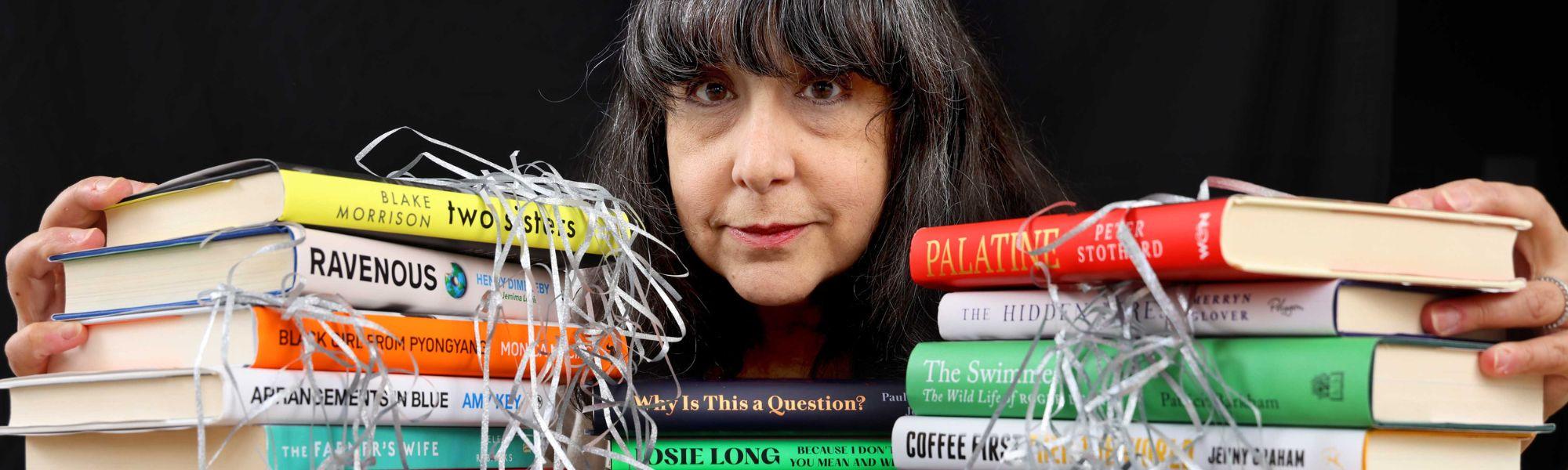 Lee Randall stands behind stacks of colourful books, only her head is visible between the books.