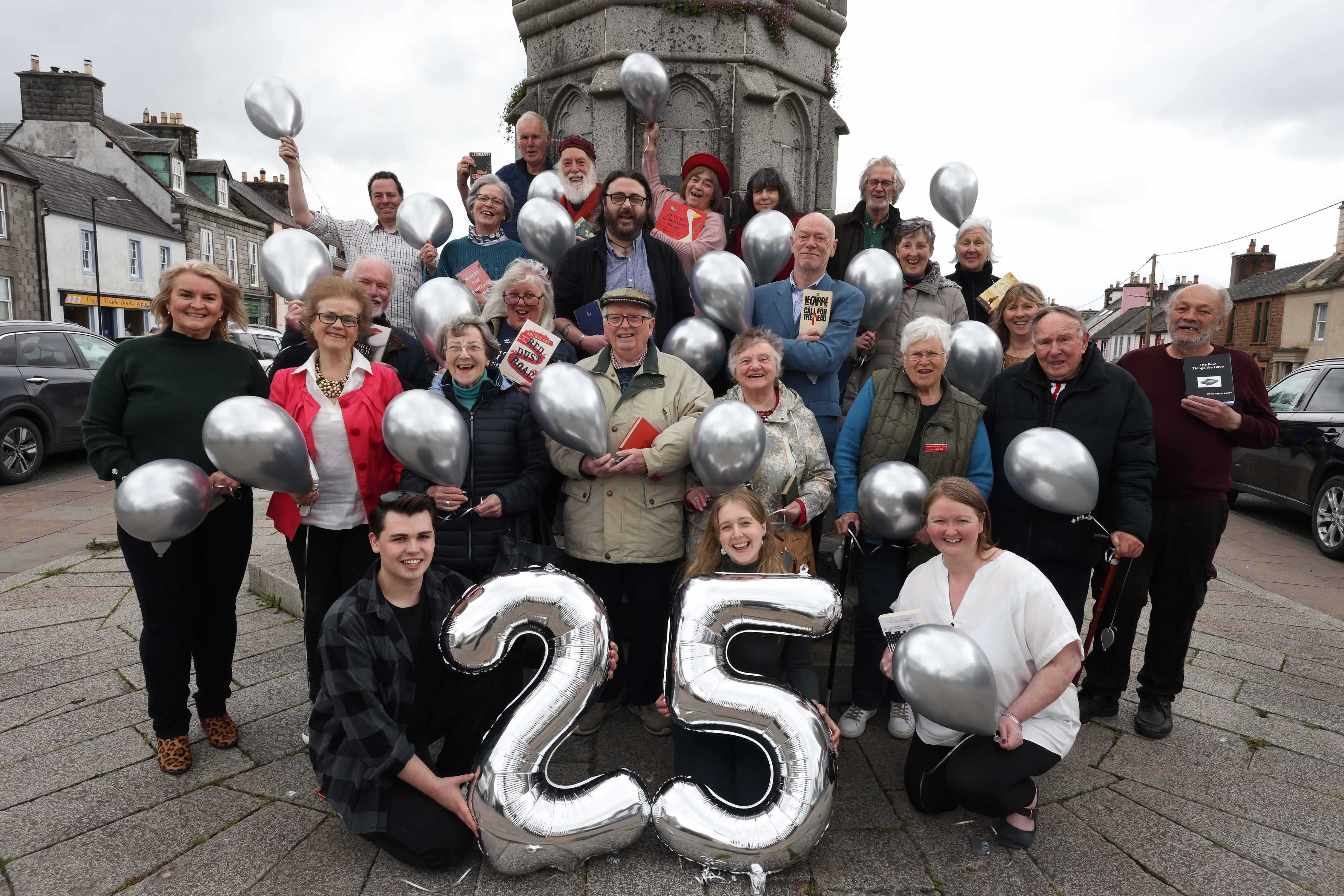 Group of people including staff, trustees and volunteer's standing in front of Mercat Cross, Wigtown holding silver balloons, to celebrate the twenty fifth anniversary of the Wigtown Book Festival.