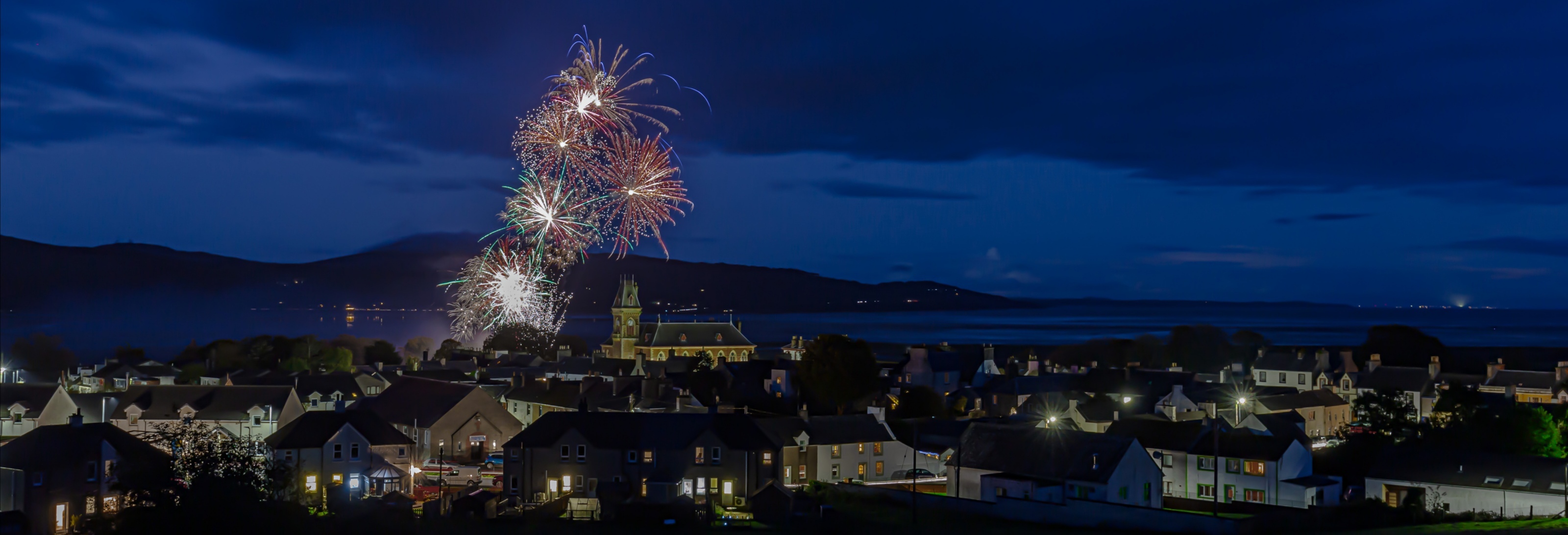 A rooftop view of Wigtown at night. Fireworks are exploding in the sky to celebrate the opening night of Wigtown Book Festival.