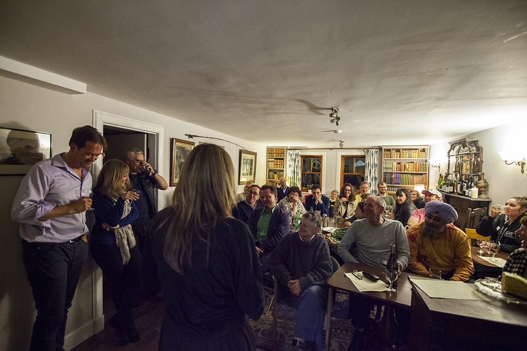 A group of people sitting in a room listening to an author at a Wigtown Book Festival event. Many of them are laughing and holding drinks in their hands.