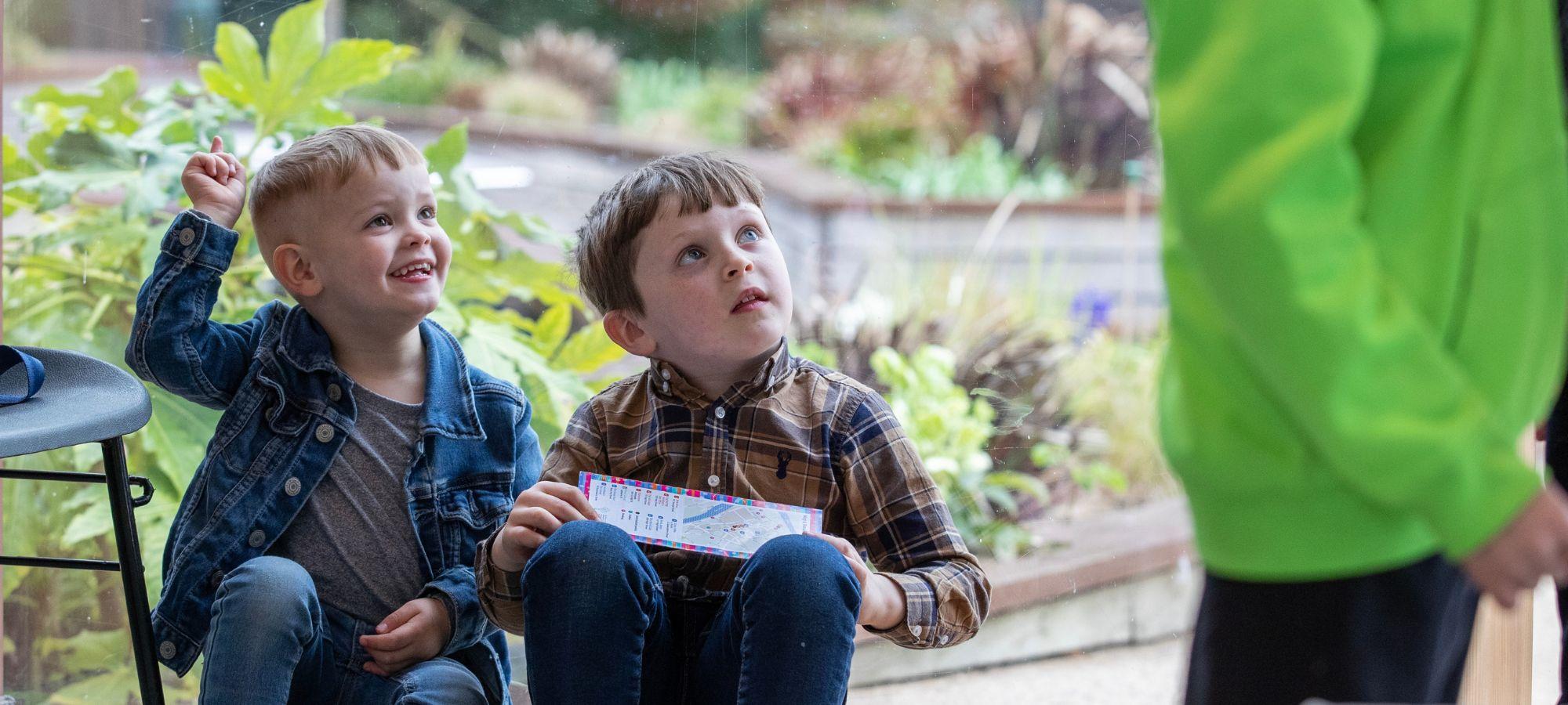 At a children's book festival event outdoors in a garden. Two children listen and interact.