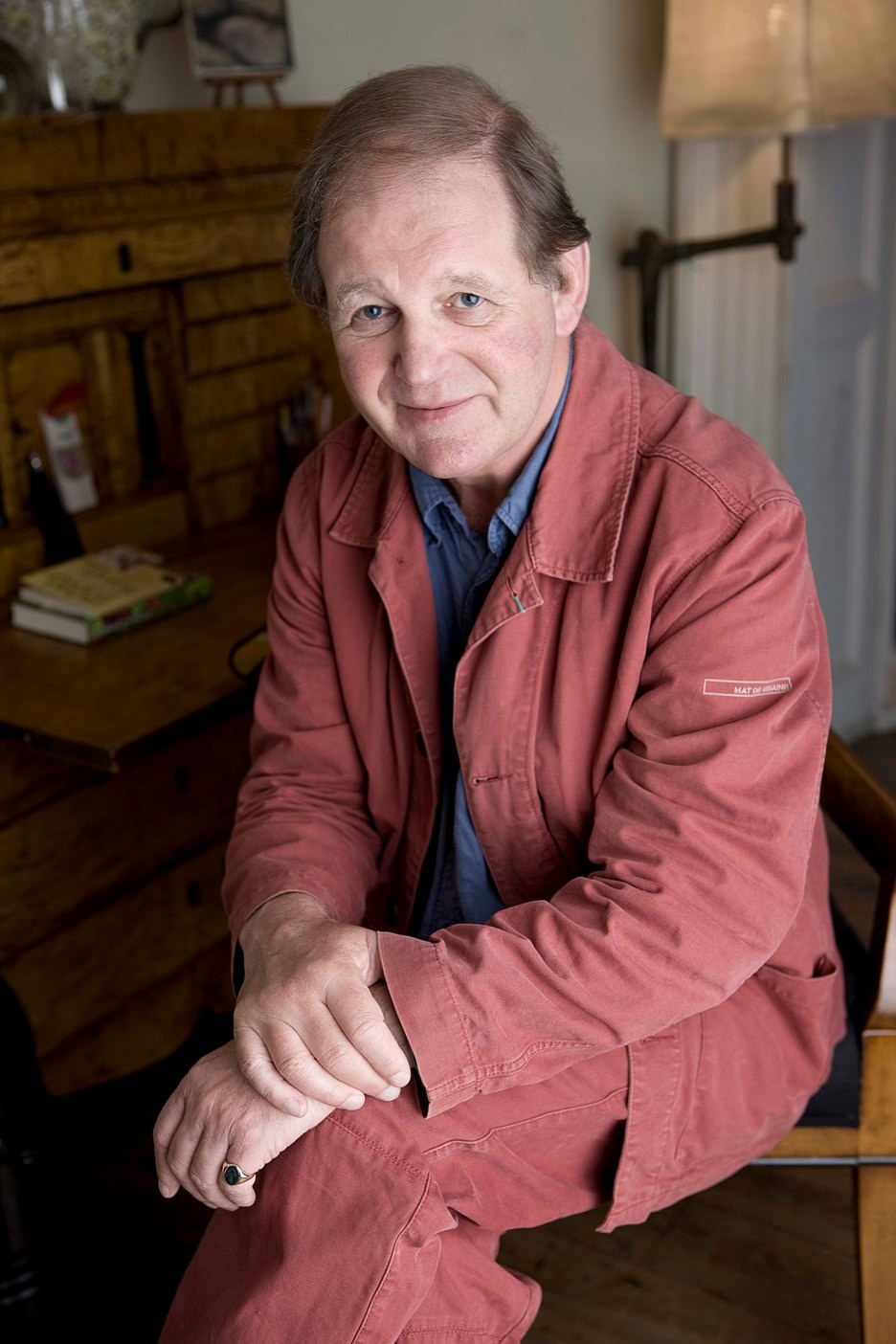 Wigtown Book Festival author Michael Morpurgo sitting at his desk, one leg crossed over the other, hands folded on his knees.