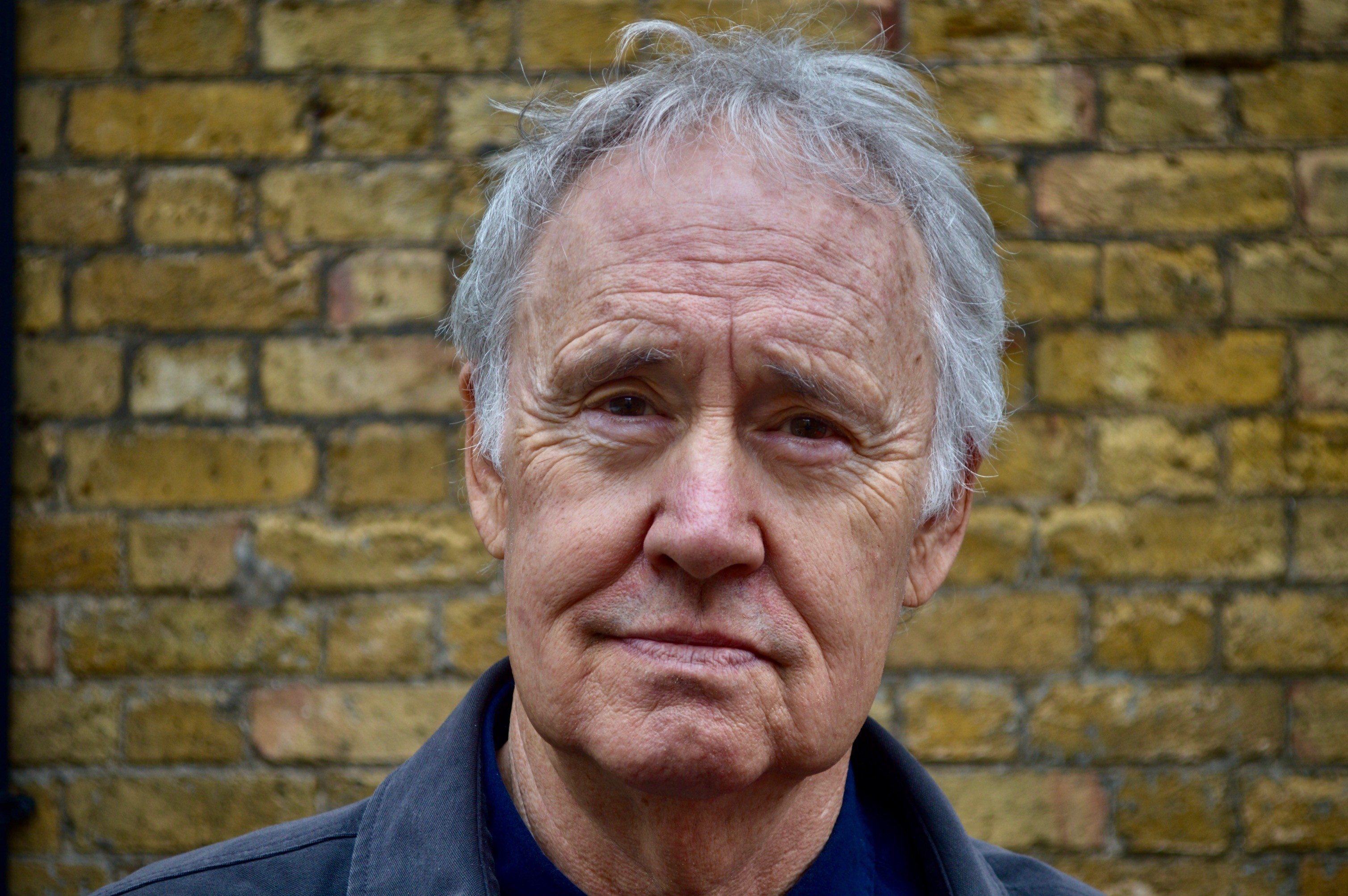 Headshot of Nigel Planer standing in front of a brick wall.