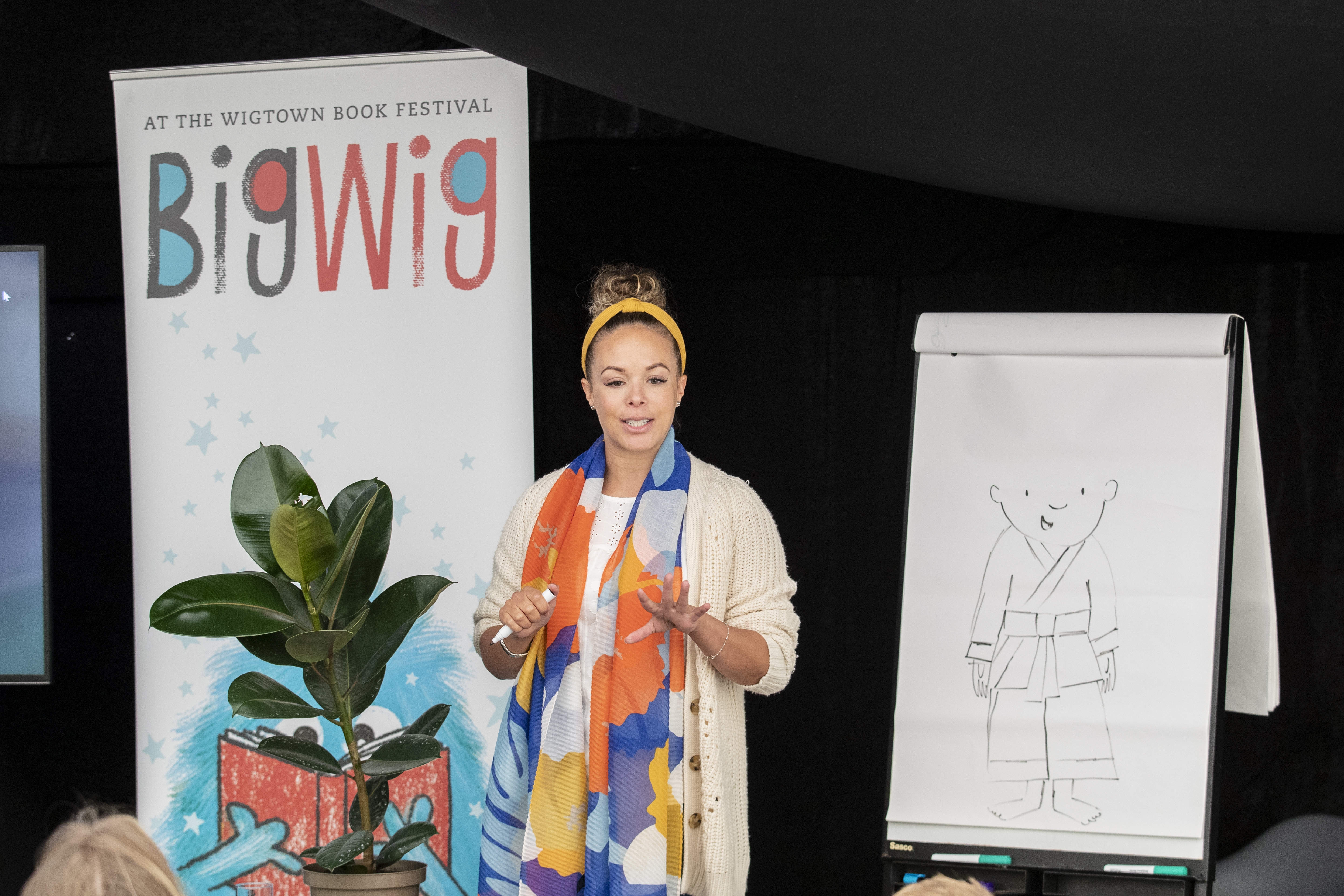 Holly Stirling on stage at her event during the Bigwig Children's Book Festival. She is standing beside a flip chart with a sketch on it.