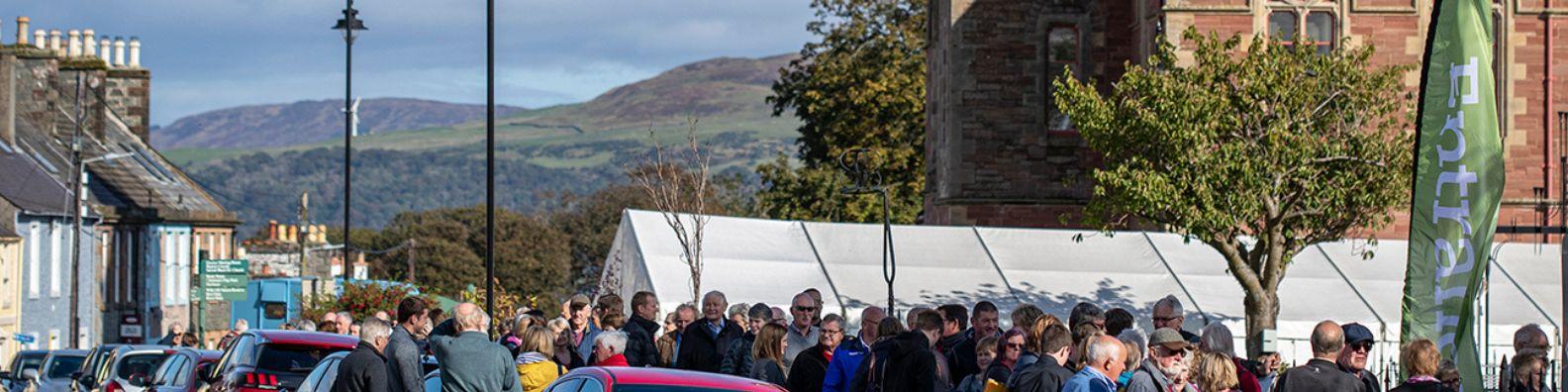 At Wigtown Book Festival, crowds queuing outside a marquee. Views to the hills beyond on a sunny autumn day.