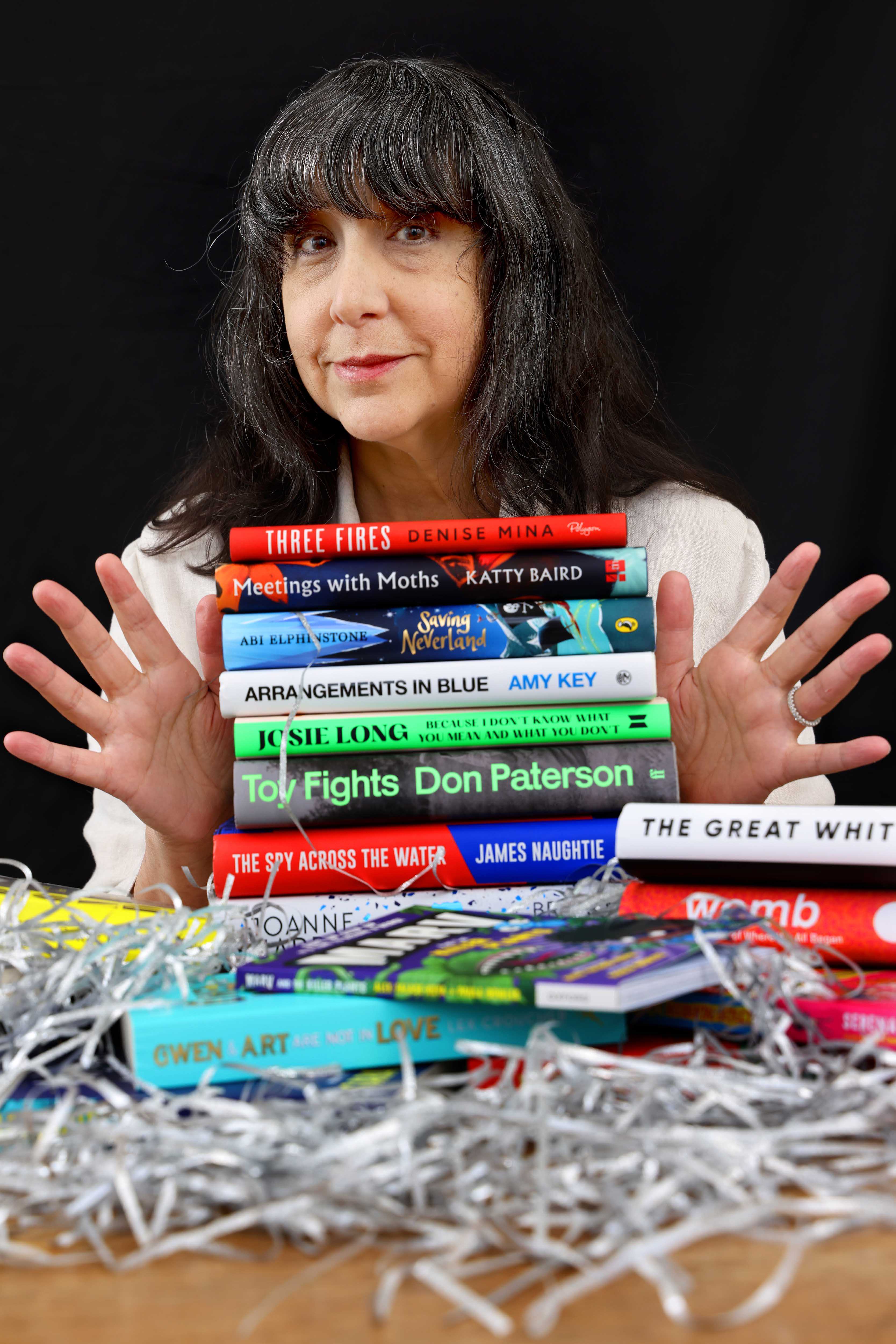 Lee Randall, Guest Programmer for Wigtown Festival Company stands behind a stack of books holding her hands out to either side of the books.