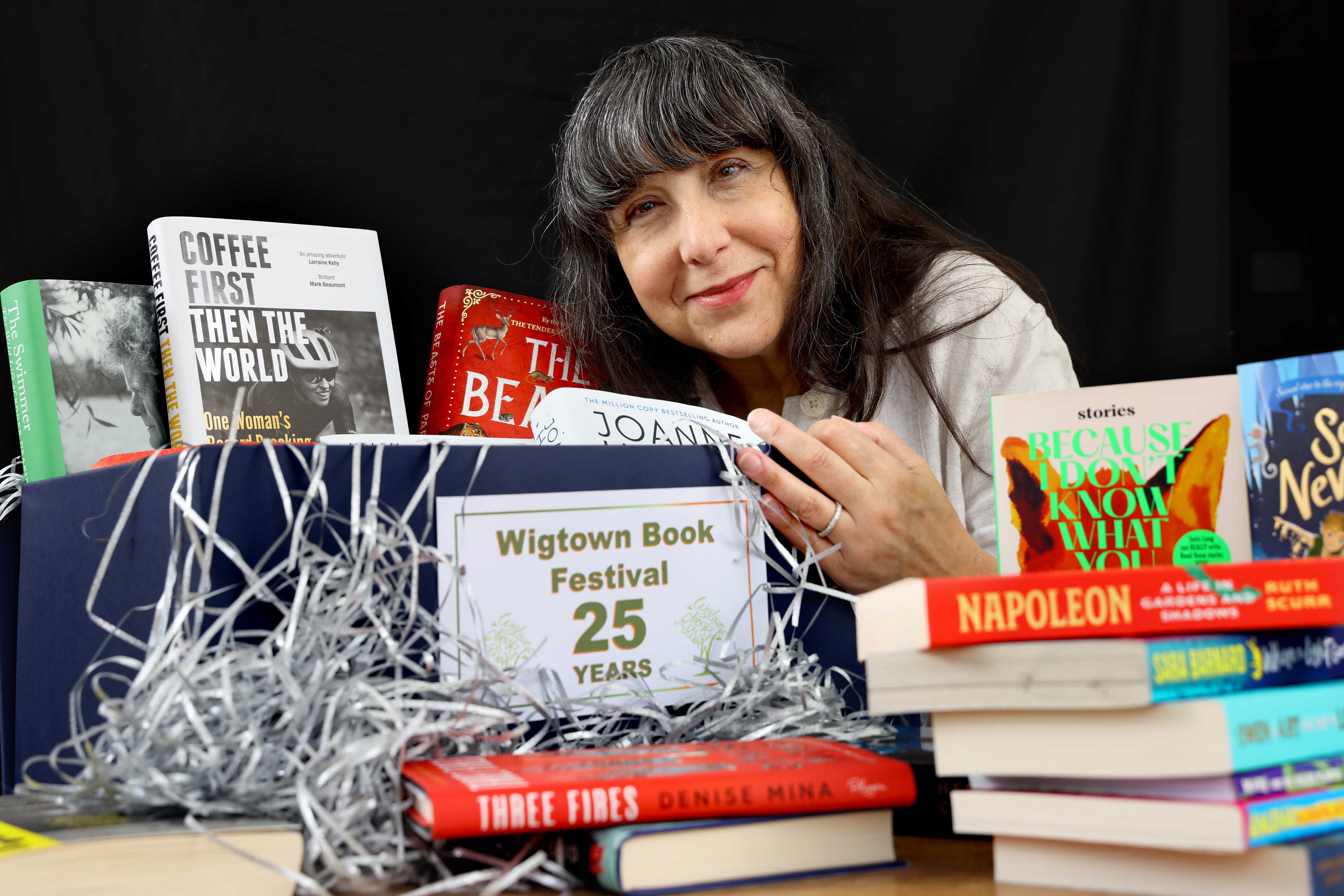 Lee Randall, Guest Programmer for Wigtown Festival Company stands behind many books placed on a table to promote the twenty fifth anniversary of the Wigtown Book Festival.