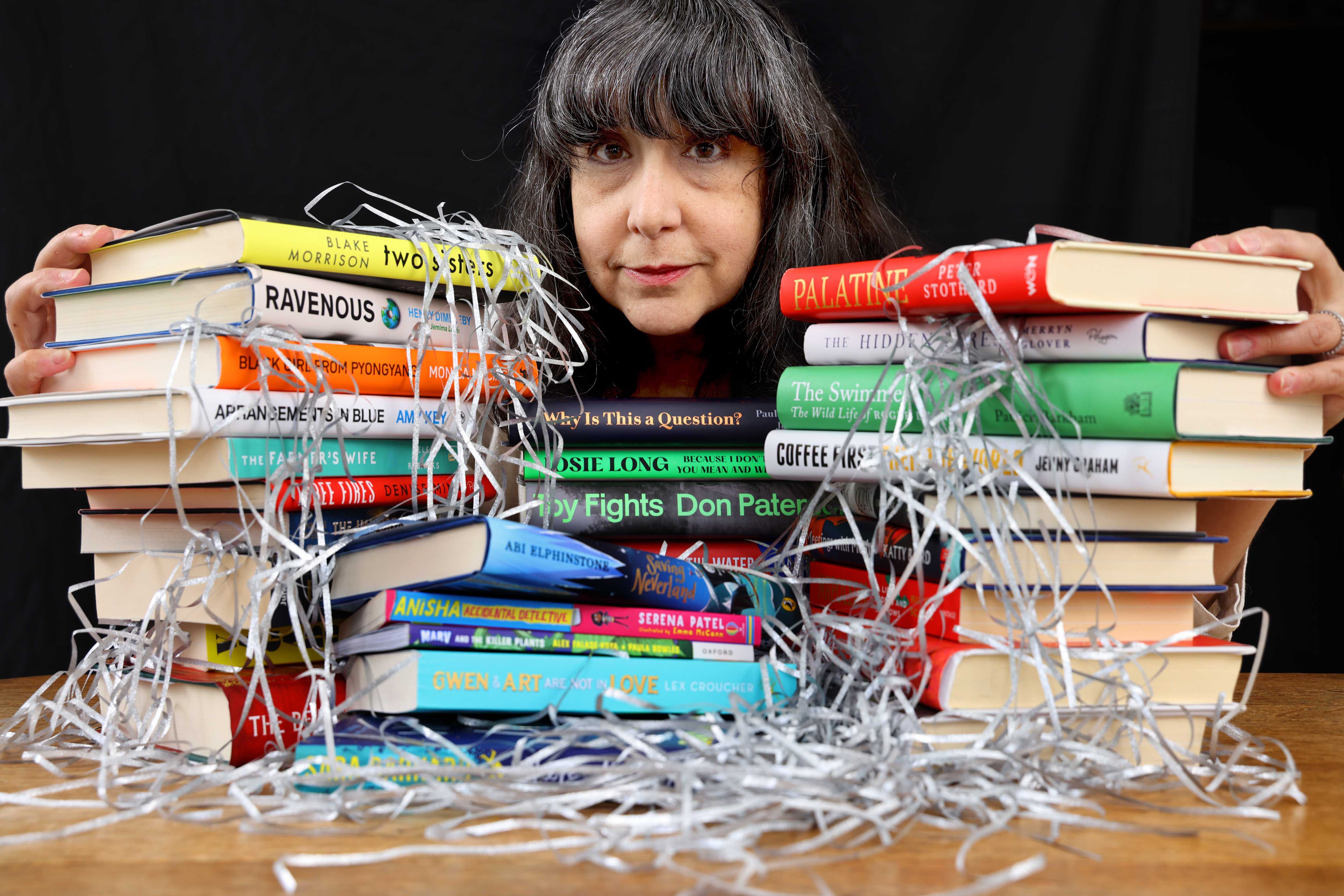 Lee Randall, Guest Programmer for Wigtown Festival Company, stands behind stacks of colourful books, only her head is visible between the books.