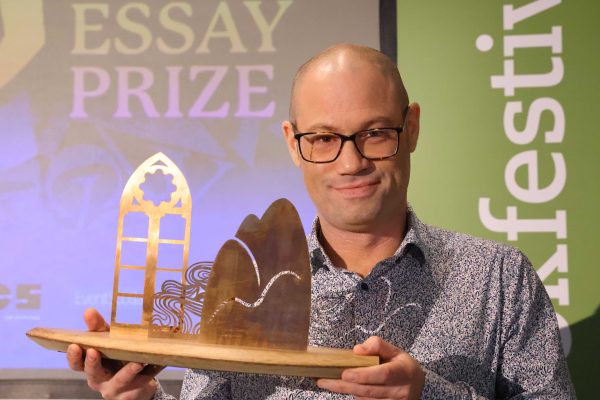 Anne Brown Prize Winner Rodge Glass holding his trophy on stage at the Wigtown Book Festival.