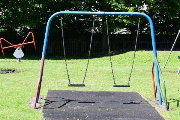 A double swing in the park at Wigtown, the sun is shining on the green grass.