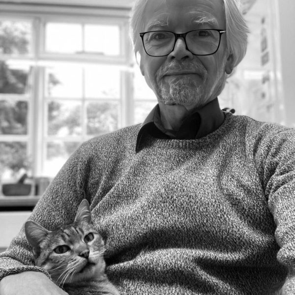 Larry Winger sitting in a chair holding a cat. Large windows behind him.