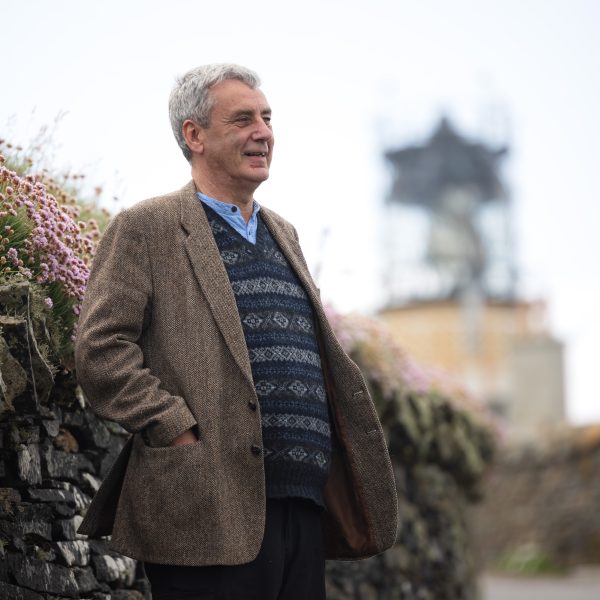 Donald S Murray standing in front of a stone wall with pink flowers.