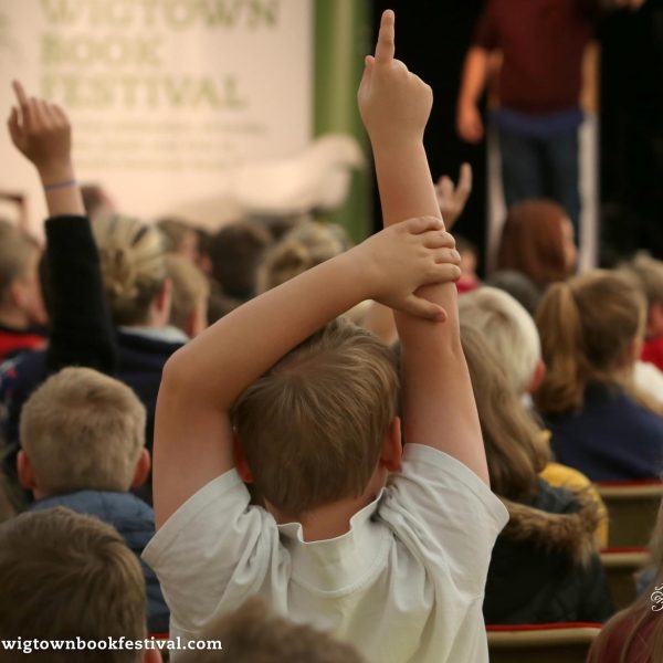 During a schools event at Wigtown Book Festival. Children in the audience raise their hands to ask a question.