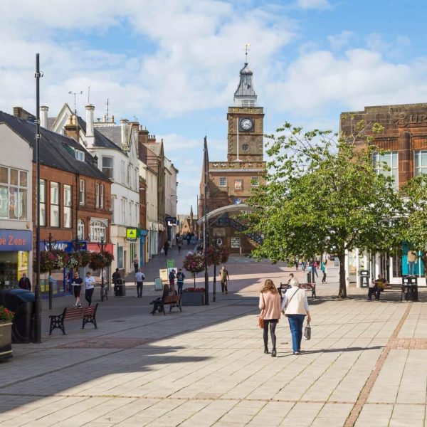 In the town centre of Dumfries, a pedestrianised area on a sunny day. Shoppers mill around.