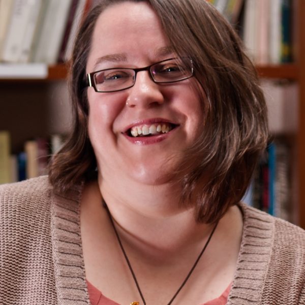 Phillipa Cochrane, trustee at Wigtown Festival Company standing in front of bookshelves full of books.