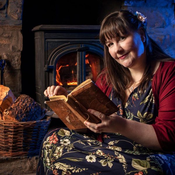 Children's author Susi Briggs sitting by a roaring fire reading a book.