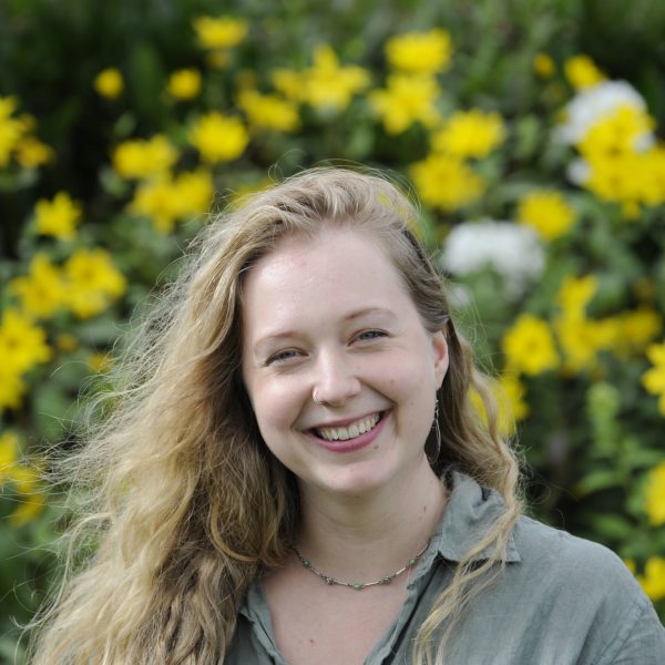 Bee Williams, Marketing and Communications Coordinator at Wigtown Festival Company standing in front of yellow flowers.