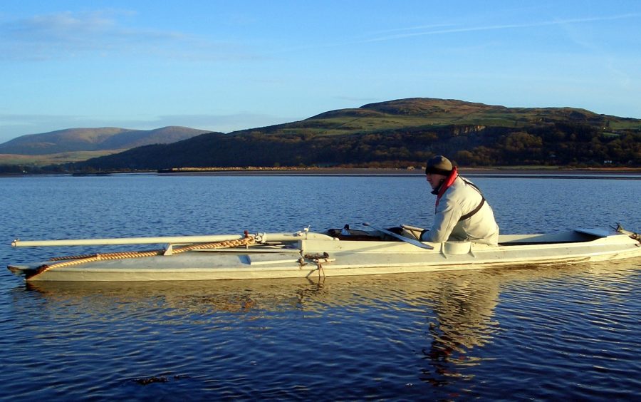 Author Peter Cockrell sitting in a punt on calm water with hills in the distance.