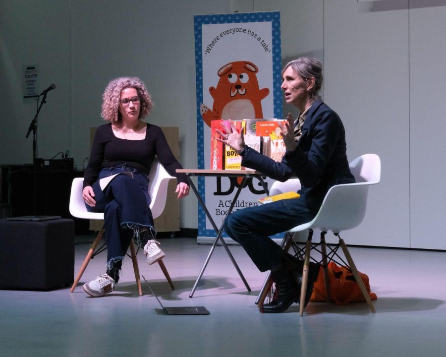 Former Children's Laureate Lauren Child at the Big DoG Schools Gala Day. She is sitting on a stage talking to the chairperson. Her hands are gesturing to the audience.