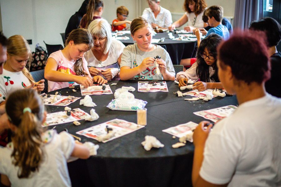 Children sitting in groups at tables making model sheep from modelling clay during a Children's Book Festival event.