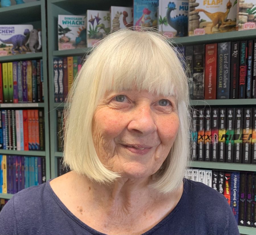 Headshot of author Donna Brewster standing in front of bookshelves full of books.